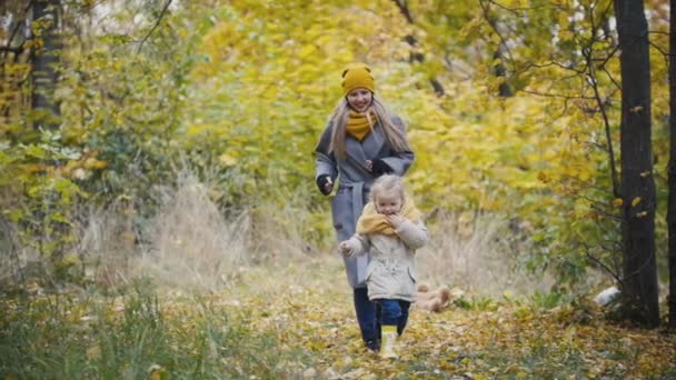 Fröhliches süßes junges Mädchen - kleine Tochter lacht und spielt Aufholjagd mit der Mutter im Herbstpark, Zeitlupe — Stockvideo