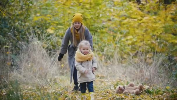 Радостная молодая девушка - маленькая дочь смеется и играет в догонялки с матерью в осеннем парке, замедленная съемка — стоковое видео