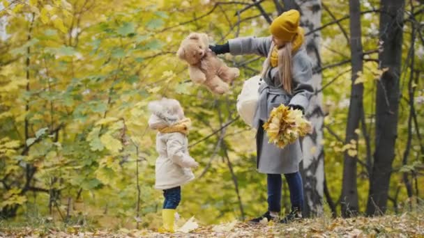 Glada lilla dotter med hennes mamma och Teddy björnen promenader i höst park — Stockvideo
