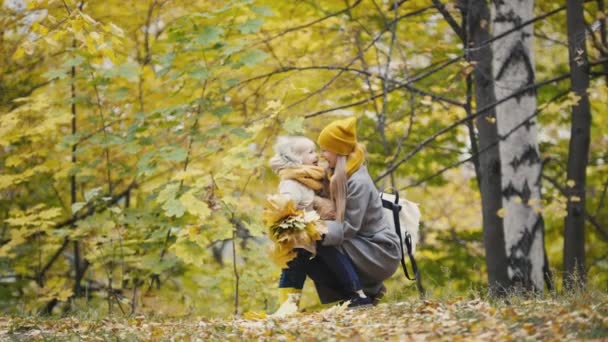 Красивая маленькая дочь со своей мамочкой гуляет в осеннем парке - поцелуй носом — стоковое видео