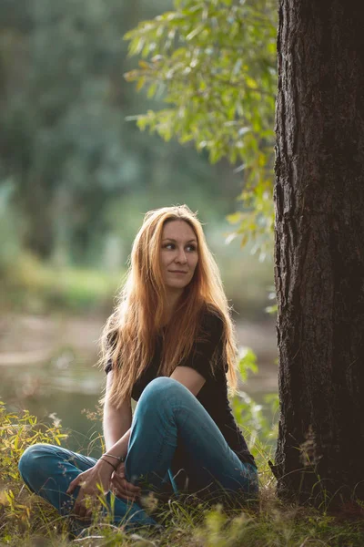 Рыжеволосая девочка, сидящая у реки в лесу, вертикальная — стоковое фото