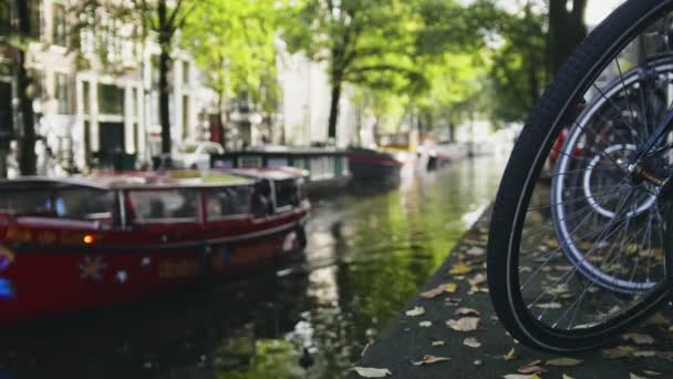 Вид на колесо велосипеда на Амстердамском канале, рядом плавает экскурсионная лодка, солнечная европейская осень — стоковое видео