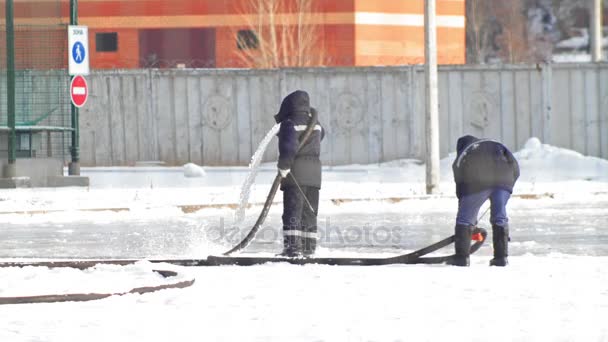 Making ice skating - two man pouring water from a hose and creates an ice skating rink — Stock Video