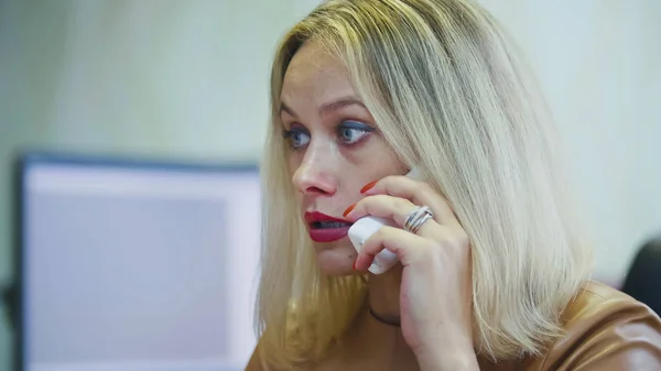 Mladá blond žena v úřadu mluvit na telefonu - před počítač, sluchátka s drátem zblízka — Stock fotografie