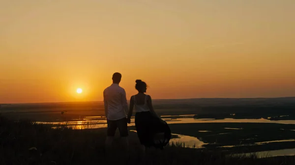 Любляча пара - хоробрий молодий чоловік і красива дівчина стоїть на високому пагорбі, шукаючи силует заходу сонця — стокове фото