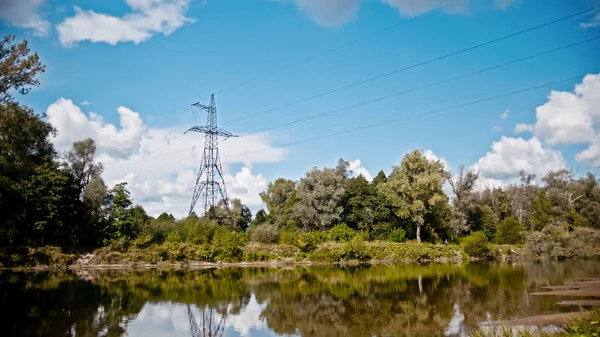 Широкий розмах електричних ліній електропередач і високовольтних пілонів на полі в сільській місцевості влітку біля річки — стокове фото