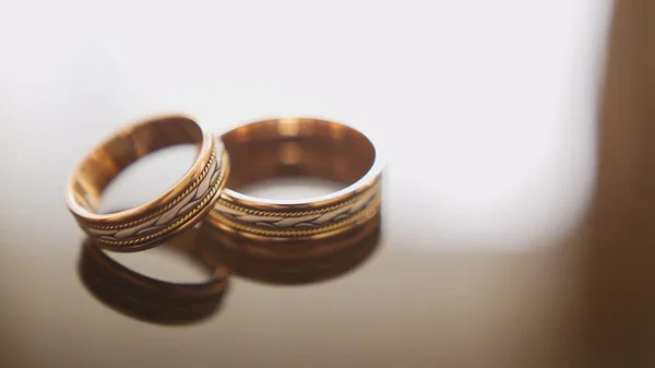 Anéis de casamento dourados na mesa de óculos de espelho - um está no topo do outro, horizontal — Fotografia de Stock