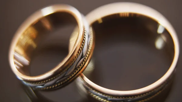 Anéis de casamento dourados na mesa de óculos de espelho - um está no topo do outro, horizontal, macro — Fotografia de Stock