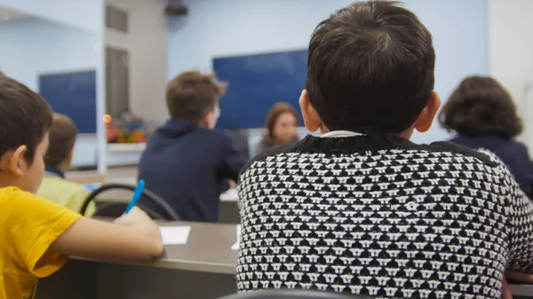 Compagni di classe bambini a scuola - ragazzo si siede a tavola e guardando durante l'insegnante spiega la lezione — Foto Stock