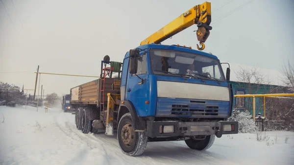 Camión de construcción con grúa amarilla en el pueblo de invierno cubierto de nieve en el día soleado — Foto de Stock