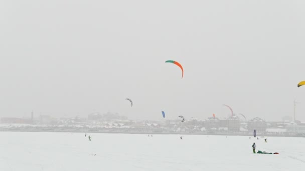 Sport estremi invernali - aquiloni colorul sul fiume di ghiaccio di fronte alla città nella giornata nuvolosa bufera — Video Stock