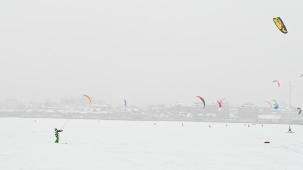 Farbenfrohe Snowdrachen auf dem Eissee vor der Stadt bei Schneesturm bewölkt, Winter Extremsport — Stockvideo