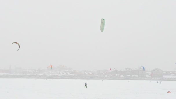 Färgglada snö-drakar sportsmens vid sjön isen framför staden på blizzard molnig dag, extremvärden vintersport — Stockvideo