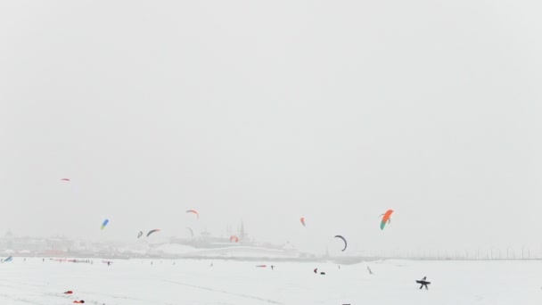 Colorido neve-pipas sobre o rio de gelo em frente à cidade em nevasca dia nublado, inverno esporte extremo — Vídeo de Stock