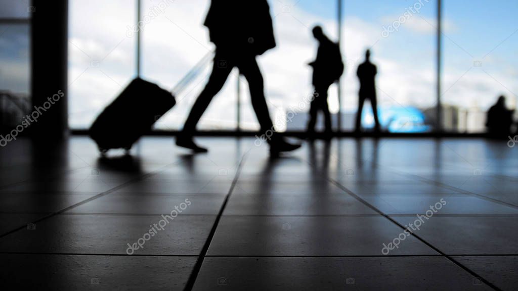 Travellers in airport walking to departures by escalator in front of window, silhouette