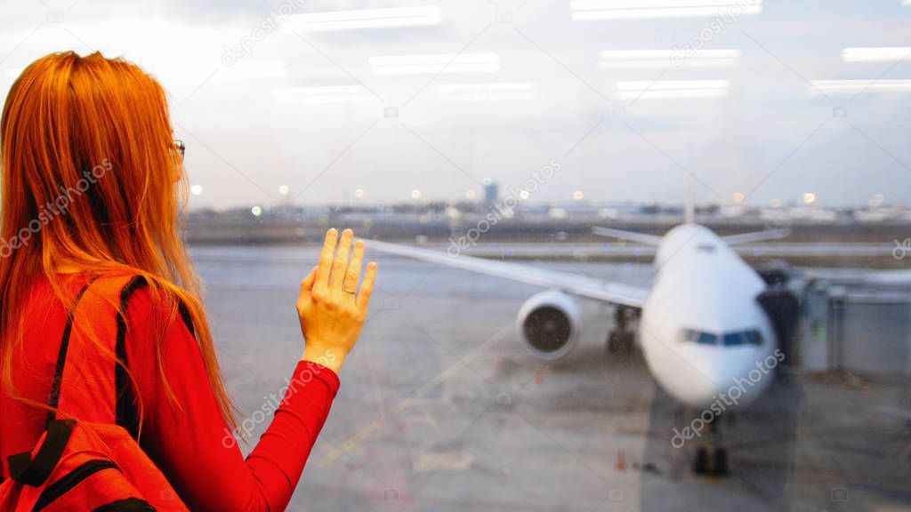 Young attractive woman with red hair and glasses looking at airplanes on runway airport