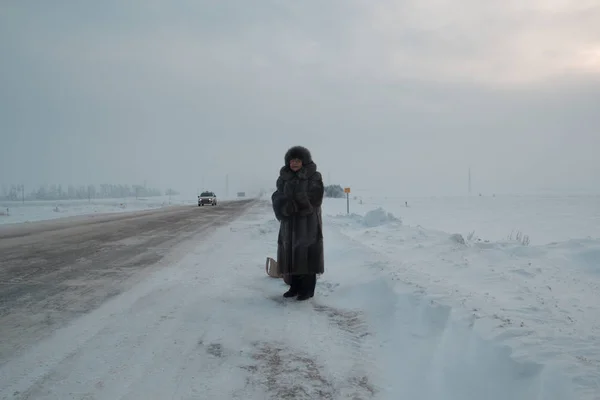 Πορτραίτο των ανώτερων γυναίκα γούνινο παλτό και καπέλο στέκεται στο χειμώνα χιόνι καλύπτονται πεδίο road, τηλεφακό — Φωτογραφία Αρχείου