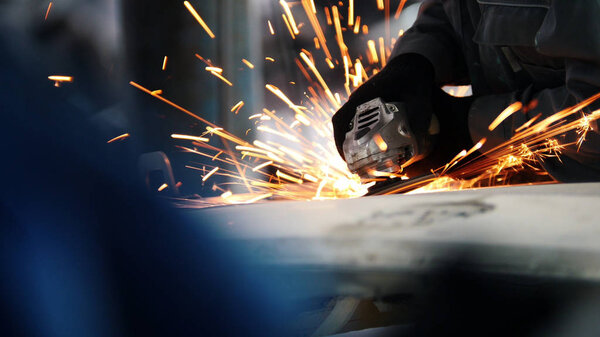 Car service - worker grinding metal construction with a circular saw