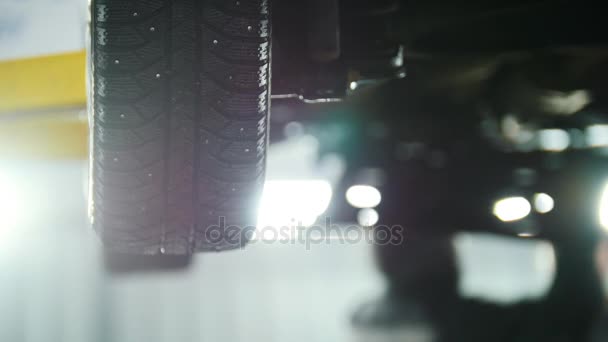 Автосервис - механик, откручивающий автомобильное устройство при работе под подъемным автомобилем, колесом — стоковое видео
