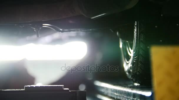 Servicio de garaje - mecánico desenroscar el dispositivo de automóvil mientras trabaja bajo un coche levantado — Vídeos de Stock