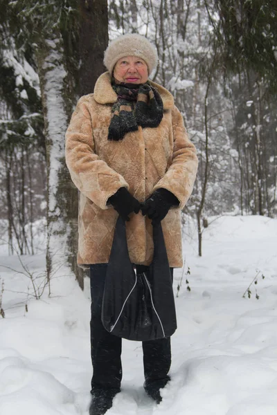 Portret van senior vrouw bontjas en hoed permanent in de koude winter besneeuwde bos, close-up — Stockfoto