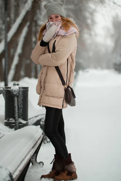 골목에 서 있는 겨울 공원에서 젊은 여자의 초상화 벤치 근처 스카프에 싸여 — 스톡 사진