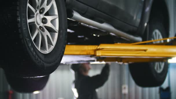 Voiture soulevée dans le service automobile pour la fixation, détail des réparations des travailleurs — Video