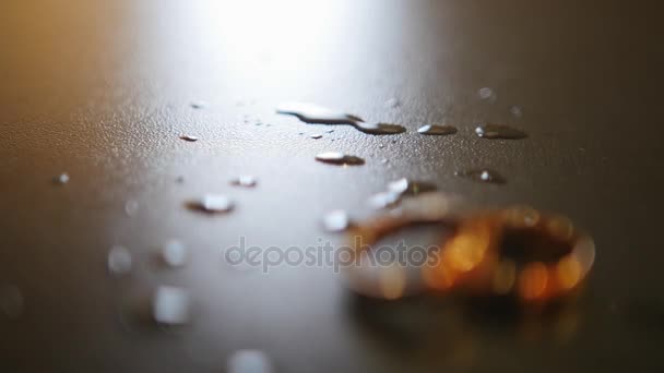 Золотые обручальные кольца на столе с капельками воды, стеллаж фокус — стоковое видео