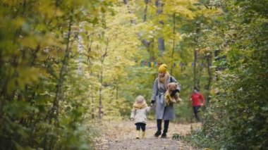Küçük sarışın kız onun anne ile sonbahar park arka sokakta, arka plan sporcular çalışır yürür