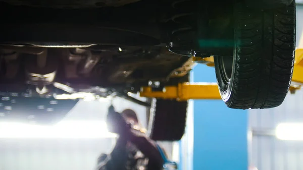Automobile diagnostic - mechanic working under a lifted car, de-focused background — Stock Photo, Image