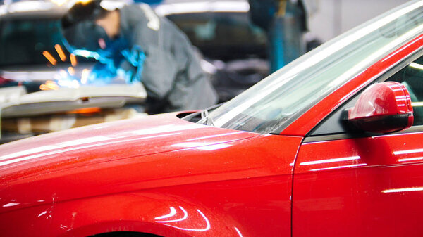 Welding industrial: worker in helmet repair detail in auto service in front of the red car