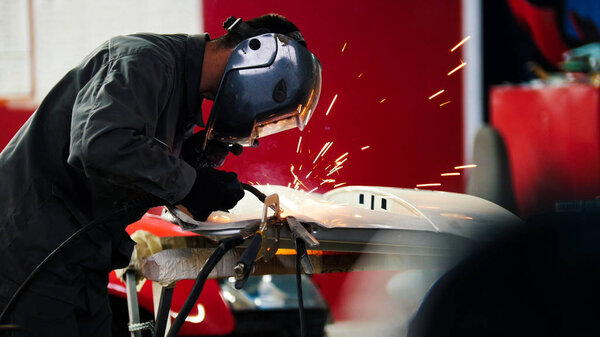 Welding industrial: worker in helmet repair detail in car auto service