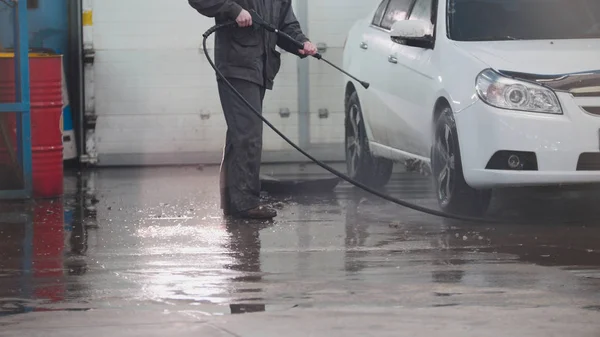 Trabajador en servicio automático está lavando un coche en las suds por mangueras de agua — Foto de Stock