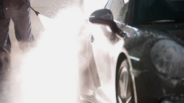 Mechaniker im Autoservice wäscht Sportwagen mit Wasserschläuchen, Hintergrundbeleuchtung — Stockfoto