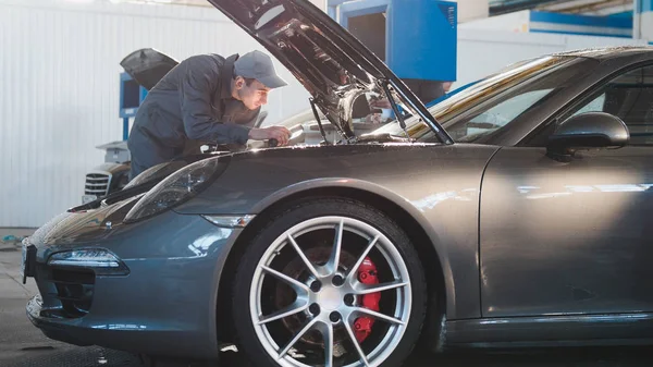Mecánico masculino en el garaje del automóvil que comprueba la capucha del coche deportivo de lujo, teleobjetivo — Foto de Stock