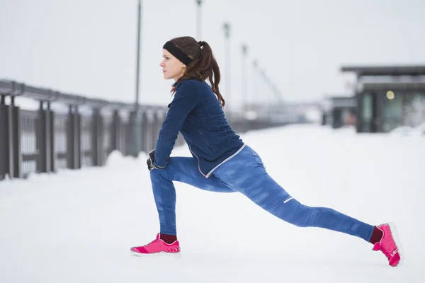 Runner młoda kobieta robi elastyczność ćwiczenia na nogi przed Uruchom przy promenadzie zima śnieg, — Zdjęcie stockowe