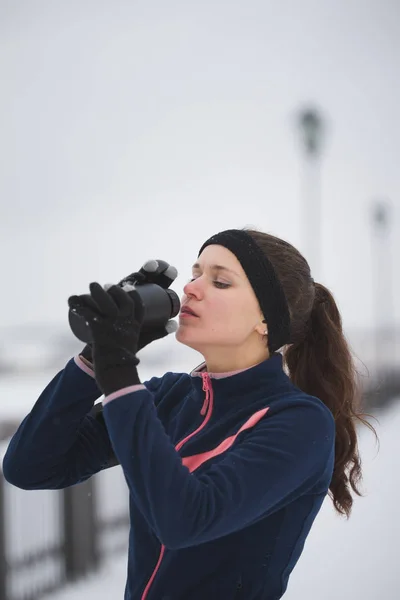 Młoda kobieta napój woda podczas joggingu poza w dzień pochmurny zimowy — Zdjęcie stockowe