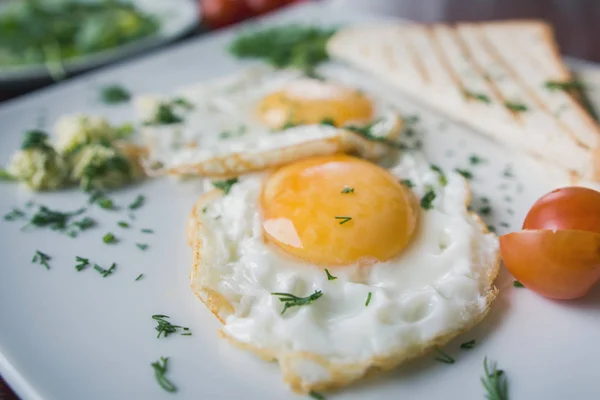 Fried eggs on white plate with green and tomato cherry - breakfast, macro view — Stock Photo, Image