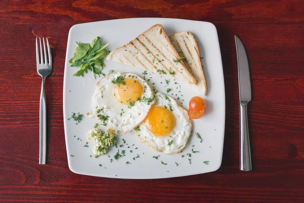 Fried eggs on white plate with green and tomato cherry - breakfast, top view — Stock Photo, Image