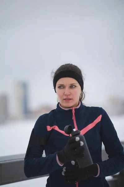 Zdrowe lifestile - młoda kobieta sportowy pić wody podczas joggingu poza w dzień pochmurny zimowy — Zdjęcie stockowe