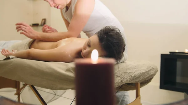 Salão de massagem - homem fazendo terapia relaxante para uma jovem, vela no quarto — Fotografia de Stock