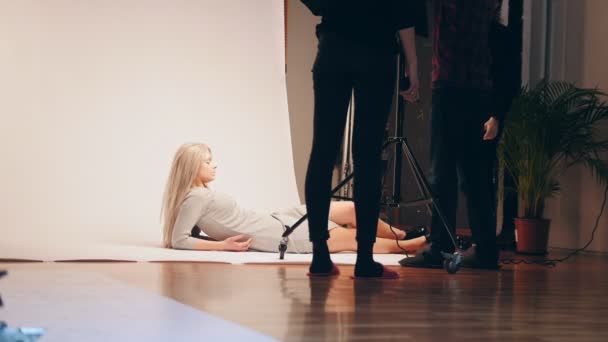 Blond meisje model liggen poseren voor de fotograaf - professionele licht in Studio — Stockvideo