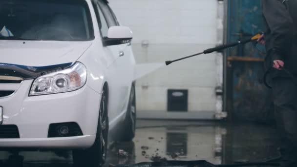 Работник автосервиса моет машину в кастрюлях водяными шлангами — стоковое видео