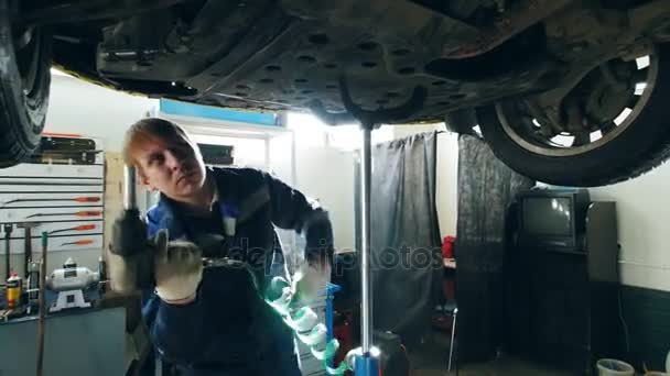 Механик откручивает детали днища машин в гаражном автосервисе, малом бизнесе — стоковое видео