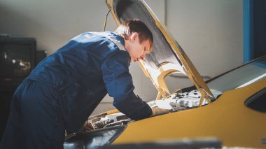 Bir mekanik elektrik, sarı araba-motor bölmesi içinde tamir başlıklı denetler