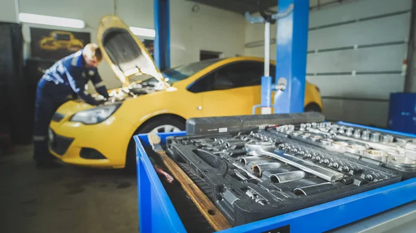 Desenfocado - un trabajador mecánico comprueba la electricidad en el capó del coche amarillo, taller de garaje — Foto de Stock