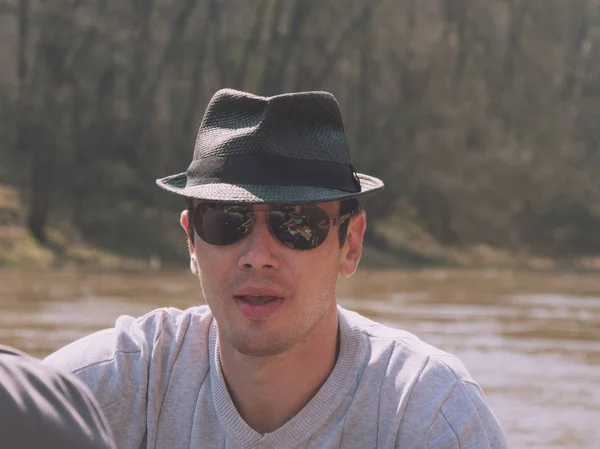 Portret van knappe Man in hoed en zonnebril in de buurt van bos rivier — Stockfoto