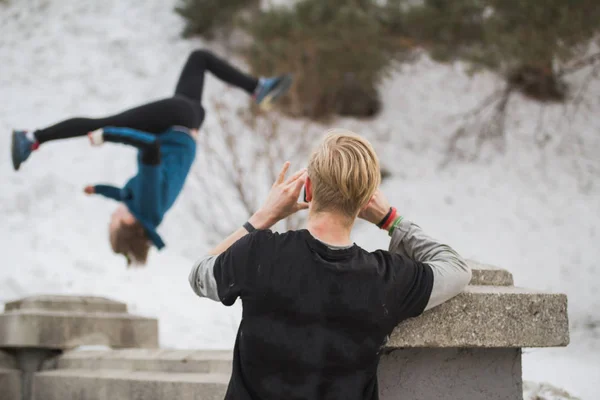 Blond włosy nastolatek sprawia, że zdjęcie na smartphone akrobyczne skok dziewczyna w zimie Park miejski-koncepcja parkour — Zdjęcie stockowe