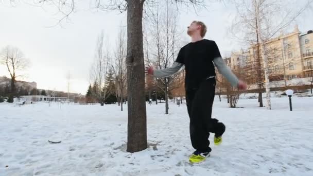 Vista en cámara lenta del atleta acróbata en el parque de invierno - ejercitar el parkour - un hombre rubio trazador salta un backflip — Vídeo de stock