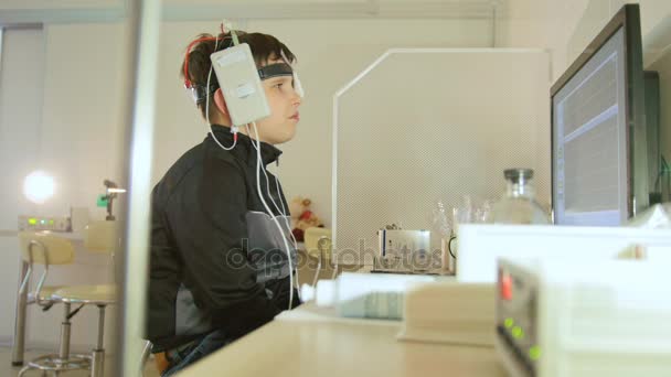 Офтальмологическая клиника исследует мальчика с электродами на голове, желающего наблюдать - диагностика медицинских детей — стоковое видео